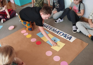 Dzieci z grupy odkrywcy układają figury geometryczne na dywanie