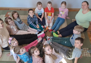 Dzieci z grupy Misie razem ze swoimi paniami siedzą w kole i pokazują kolorowe skarpetki.