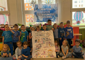 Motylki pozują ubrani na niebiesko na tle dekoracji z okazji Światowego Dnia Świadomości autyzmu trzymając wykonany przez siebie plakat.