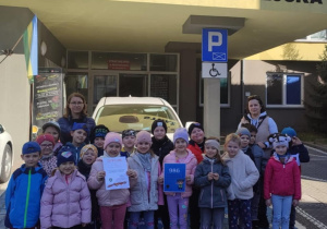 Dzieci z grupy Pszczółki pozują do zdjęcia przed budynkiem Straży Miejskiej.