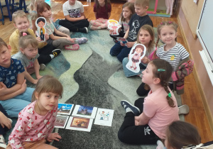 Dzieci z grupy Smerfy pozują do zdjęcia z obrazkami tematu „Zwiedzanie miasta” z kukiełkami.