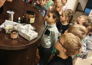 Dzieci stoją przed ladą i słuchają opowieści o kosmetykach.