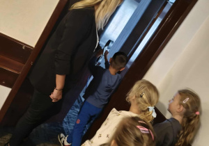 Dzieci stoją w kolejce i po kolei otwierają drzwi do pokoju hotelowego.