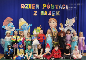Dzieci z grupy Żabki pozują do zdjęcia grupowego na tle dekoracji ,,Dzień Postaci z Bajek”.