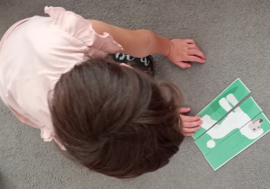 Dziewczynka siedzi na dywanie i układa puzzle.