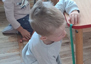 Dzieci z grupy Stokrotki ćwiczą mierzenie stolika za pomocą miary krawieckiej.