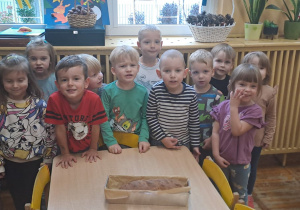Dzieci z grupy Misie pozują do zdjęcia, gdzie na stoliku leży blaszka z upieczonym chlebem przez grupę.