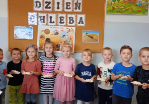 Dzieci z grupy Liski prezentują własnoręcznie wykonane bułeczki z masy solnej. W tle tablica z dekoracją z okazji Dnia Chleba.