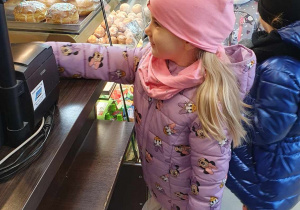 Dziewczynka ubrana na różowo kupuje w piekarni bułką.