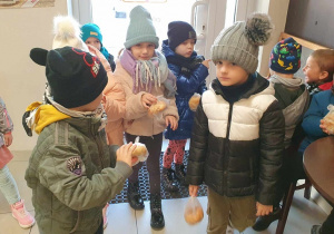 Dzieci oglądają bułki zakupione przez siebie w piekarni.