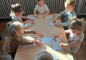 Dzieci przy stoliczku przyklejają znaczki pocztowe do koperty.