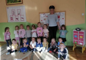 Dzieci z grupy ,,Misie” pozują do zdjęcia na tle tablicy dekoracyjnej wraz z zaproszonym gościem - mamą dziewczynki z grupy , która pracuje na Poczcie Polskiej.