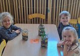 Dzieci siedzą przy stoliku ze swoimi pracami „Las w słoiku”.
