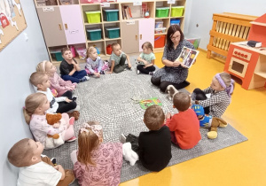 Nauczycielka pokazuje dzieciom siedzącym w kole książkę o psach.