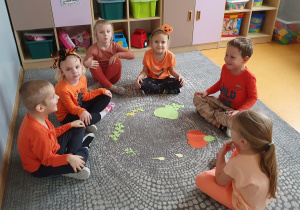 Dzieci siedzą na dywanie w kole prezentują stworzony przez siebie Cykl Życia Dyni