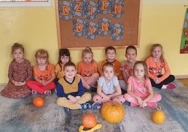 Dzieci z grupy Słoneczka siedzą na dywanie pod tablicą z napisem Dzień Dyni, a przed nimi ułożone są dynie.
