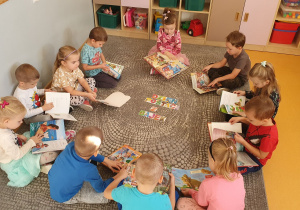 Dzieci siedzą na dywanie i przeglądają przyniesione przez siebie książki. Na środku widać napis „Dzień Postaci z Bajek”.