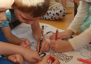 Dzieci wspólnie kolorują malowankę.