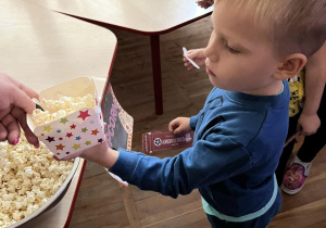 Chłopiec daje nauczycielce kupon na popcorn w zamian dostaje kubeczek smakołyków.