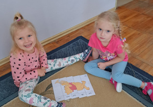 Dwie dziewczynki układają puzzle „Kubuś Puchatek”.
