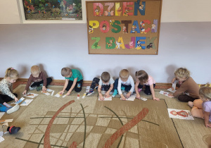 Dzieci siedzą na dywanie, układają puzzle przedstawiające bohaterów baśni i bajek.