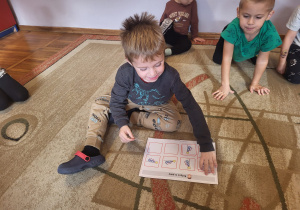 Chłopiec siedzi na dywanie, dobiera obrazki w pary.