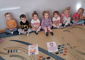 Dzieci z grupy Biedronki siedzą na dywanie i oglądają zdjęcia swoich ulubionych bajkowych bohaterów.
