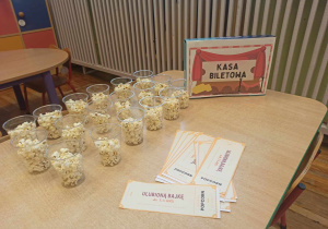 Zdjęcie przedstawia napis „Kasa Biletowa” oraz bilety do kina i popcorn, które dzieci zakupią na seans filmowy, zorganizowany w sali przedszkolnej.