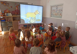 Dzieci z grupy Biedronki siedzą w kinie zorganizowanym w sali przedszkolnej i oglądają swoją ulubioną bajkę.
