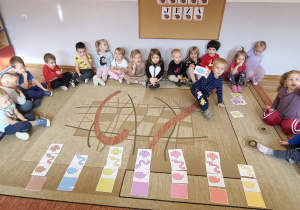 Dzieci siedzą na dywanie, dobierają jeżyki i inne emblematy do odpowiedniego koloru.