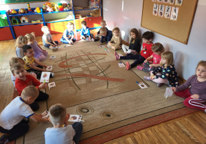 Dzieci siedzą na dywanie, wyszukują i zaznaczają za pomocą klamerki takiego samego jeżyka jak we wzorze.