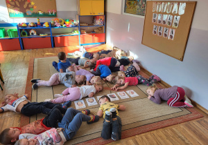 Dzieci leżą na dywanie, wykonują czynności zgodne z opowieścią ruchową.