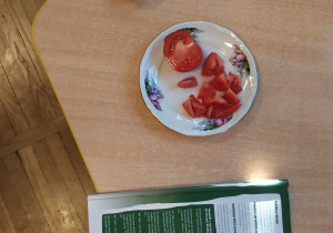 Zdjęcie przedstawia całego oraz pokrojonego pomidora na małe kawałki oraz materiały dydaktyczne związane z projektem