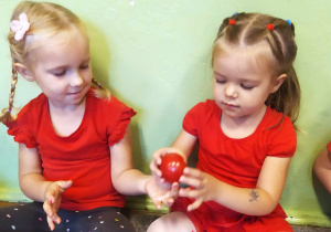 Dwie dziewczynki ubrane w czerwone koszulki przyglądają się jak wygląda pomidor