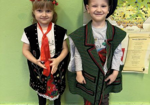 Dziewczynka i chłopiec stoją uśmiechnięci przebrani w tradycyjny strój opoczyński.
