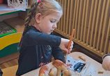 Dziewczynka siedzi przy stoliku i maluje brązową farbą plakatową swoje grzybki.