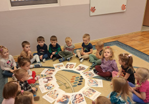 Dzieci grupy Biedronki siedzą na dywanie z planszami przedstawiającymi Prawa Dziecka.