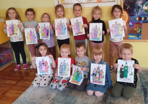 Dzieci z grupy Słoneczka trzymają przed sobą malowanki z pokolorowanymi kredkami.