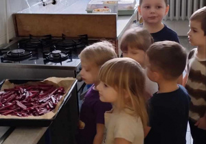 Dzieci stoją w przedszkolnej kuchni i przygotowują frytki z buraków.