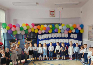Dzieci z grupy „Biedronki” stoją odświętnie ubrane i pozują do zdjęcia na tle dekoracji „Pasowanie na Przedszkolaka”.
