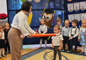Pani Dyrektor kładąc na lewym ramieniu dużą kredkę pasuje chłopca z grupy „Biedronki” na przedszkolaka.