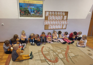 Dzieci siedzą na dywanie, przytulają misie.