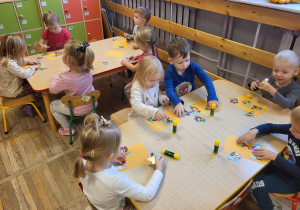 Dzieci siedzą przy stolikach, układają puzzle z misiem.