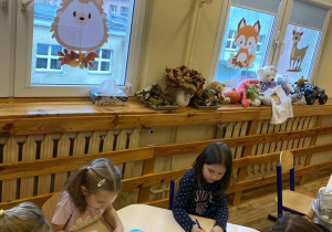 Dziewczynki siedzą przy stoliku i kolorują swoje zakładki używając mocnych kolorów.