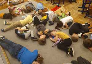Dzieci leżą na dywanie i przytulają swoje misie.
