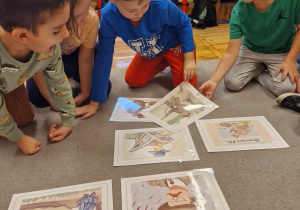 Dzieci siedzą na dywanie i układają historyjkę obrazkową.