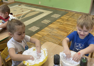 Chłopiec i dziewczynka na zdjęciu mieszają w miskach piankę do golenia z mąką ziemniaczaną.