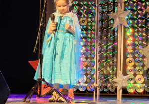 Na zdjęciu widzimy dziewczynkę, która śpiewa na scenie.