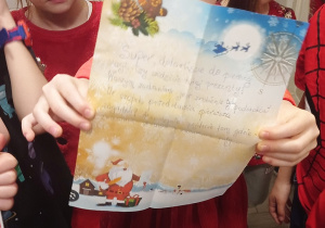 Zdjęcie przedstawia dzieci stojące w łazience, na pierwszym planie stoi dziewczynka, która trzyma drugi list od św. Mikołaja znaleziony w przedszkolnej łazience.