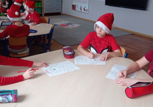 Zdjęcie przedstawia dzieci siedzących przy stolikach. Przedszkolaki wykonują pracę plastyczną o tematyce świątecznej.